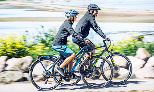 En mand og en kvinde cykler på trekkingcykler langs havet.