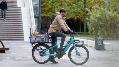 En cyklist kører gennem bymidten på sin blå Cube Longtail. Han har en kasse med dagligvarer stående på bagagebæreren.