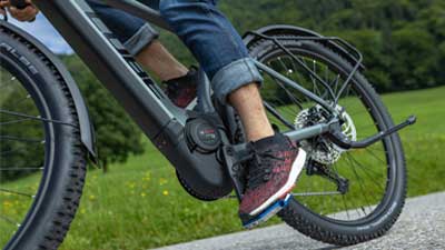 Billedet viser et nærbillede af en grå Cube Reaction Hybrid Allroad-cykel. Man ser nærmere på pedalakslen samt elcykelens motorblok under kørslen.