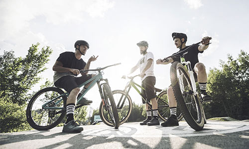 Tre freestyle-cyklister står ved deres cykler og snakker sammen på en solskinsdag
