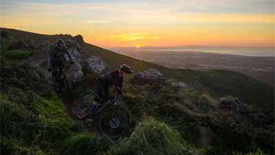 To cyklister kører ned ad en bakke, hver på en Cube Stereo Fully-mountainbike.