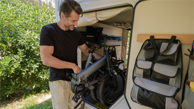 En mand lægger sit sammenklappede foldecykel i en autocamper.