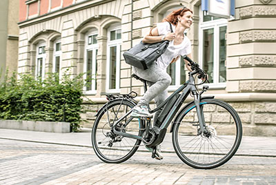 En kvinde cykler gennem bymidten med en håndtaske under armen på en Winora-cykel.