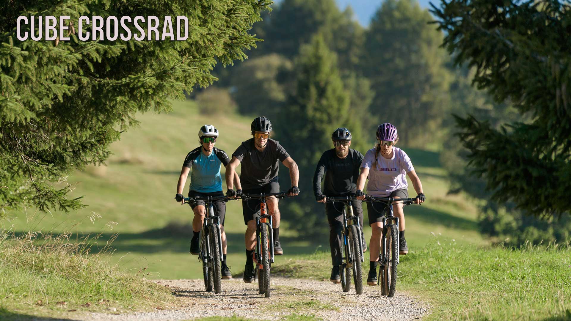 Man ser en gruppe cyklister, der kører ad en skovvej. Billedet er forsynet med titlen »Cube Crosscykel
