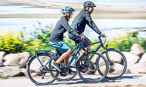 En mand og en kvinde cykler på trekkingcykler langs havet.