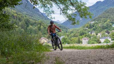 En cyklist kører på sin mountainbike ad en grusvej, med et bjergrigt landskab i baggrunden.