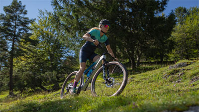 Man ser en cyklist på sin mountainbike. Hun cykler gennem et kuperet terræn.