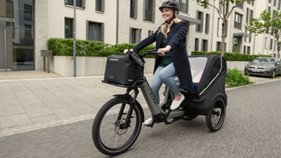 En kvinde cykler gennem et boligkvarter på en grå ladcykel.