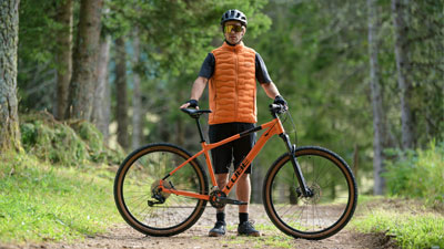 En mand står bag sin orange Cube-mountainbike på en skovvej.