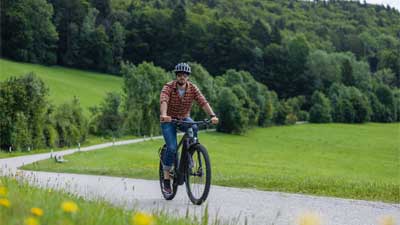 En cyklist kører på sin mountainbike ad en asfalteret cykelsti, med et landskab i baggrunden.