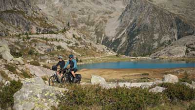 Et par cykler på trekkingcykler gennem et stenet landskab, med bjerge og en sø i baggrunden.