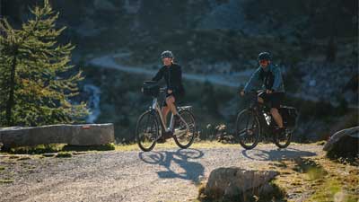 Et par cykler på mountainbike på en cykelsti, med et bjergrigt landskab i baggrunden.