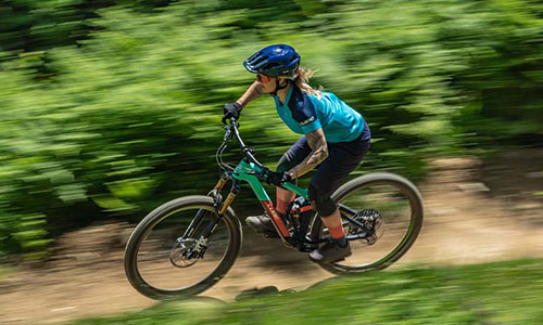 Man ser en kvinde på en mountainbike, der kører hurtigt ad en skovvej.