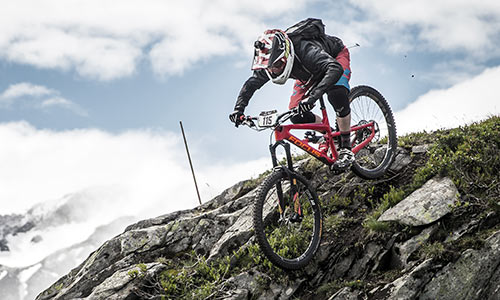 En downhill-cyklist med fuldhjelm kører ned ad en stenet bjergside over klipper.
