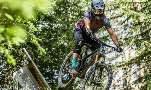 En cyklist med fuldhjelm kører på en fuldt affjedret mountainbike gennem skoven.
