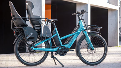 Her ses en blå Cube Longtail Hybrid-lastcykel med to udstyrede børnesæder. 