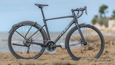 Man ser en sort Cube Gravel Bike, der står i et klippefyldt landskab, med kysten i baggrunden.
