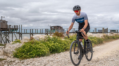 Man ser en mand i cykeltøj. Han kører på sin gravelcykel ad en strandvej.