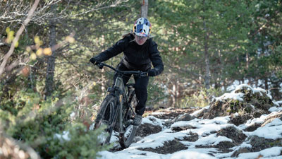 En cyklist kører på sin mountainbike gennem den ujævne skov, hvor jorden nogle steder stadig er dækket af sne.