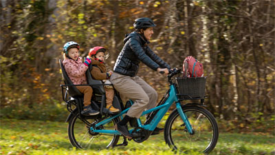 På billedet ses en mor på en blå Cube Longtail-lastcykel. På bagagebæreren sidder to småbørn.