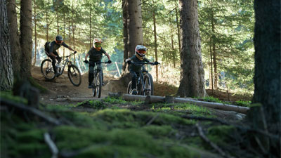 To unge og en cyklist kører gennem skoven på Cube Stereo Fully-mountainbikes.